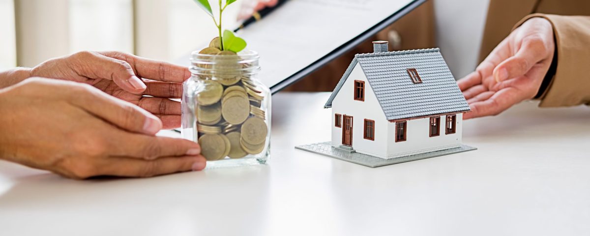 A jar filled with coins growing a small plant beside a model house, symbolizing saving, mortgage planning, and personal loan decisions.