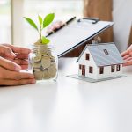 A jar filled with coins growing a small plant beside a model house, symbolizing saving, mortgage planning, and personal loan decisions.