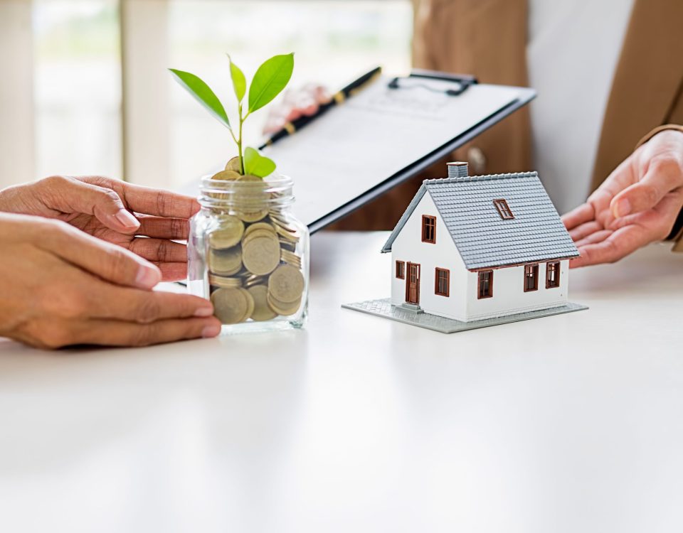 A jar filled with coins growing a small plant beside a model house, symbolizing saving, mortgage planning, and personal loan decisions.